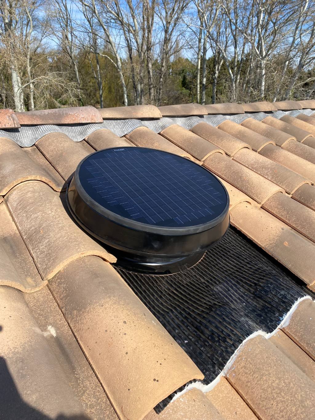 Extracteur solaire à panneau intégré, vu en entier sur une toiture en tuiles